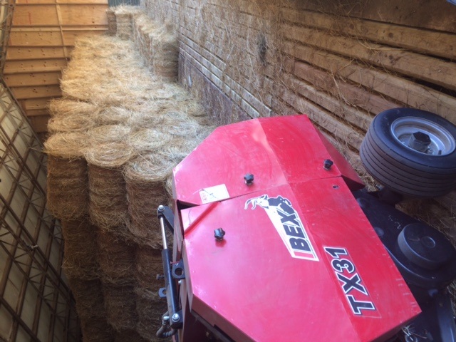 Ibex TX31T Mini Round Baler with twine wrap with its produced mini round hay bales stacked in a barn for storage. 